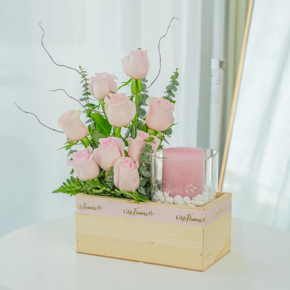 A wooden box arrangement of 9 pink roses with eucalyptus leaf and Pink Scented Candle in vase.