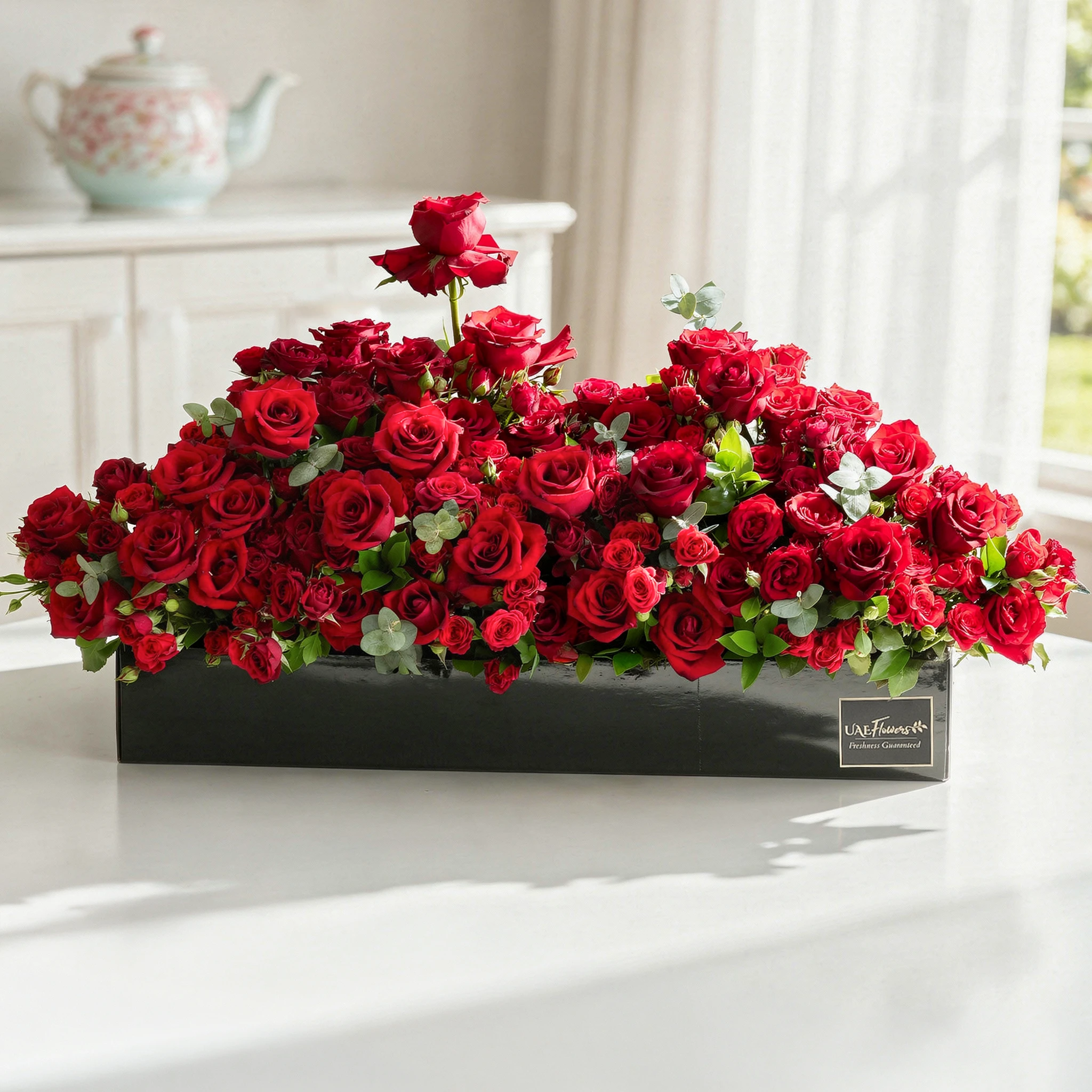 Arrangement of 50 red roses and 30 red spray roses with green fillers in a long black box. Arrangement of 50 red roses and 30 red spray roses with green fillers in a long black box.