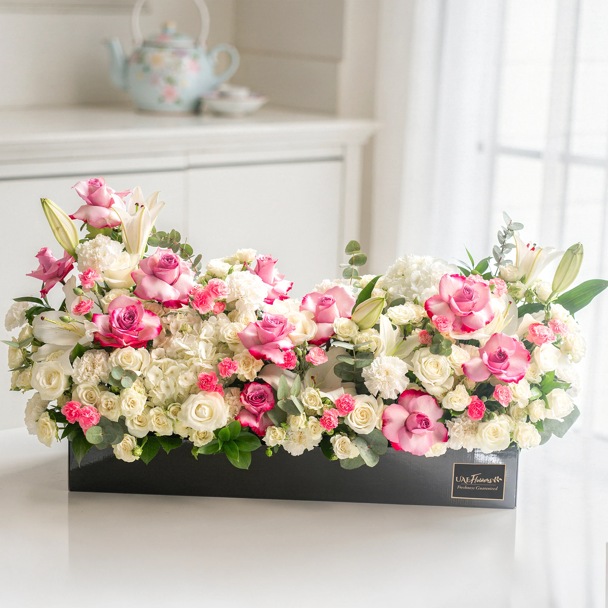 Arrangement of 5 white lilies, 15 purple roses, 15 white roses, 10 white carnations, 10 pink carnations, 10 white spray roses and 2 white hydrangeas with green fillers in a long black box. Arrangement of 5 white lilies, 15 purple roses, 15 white roses, 10 white carnations, 10 pink carnations, 10 white spray roses and 2 white hydrangeas with green fillers in a long black box.