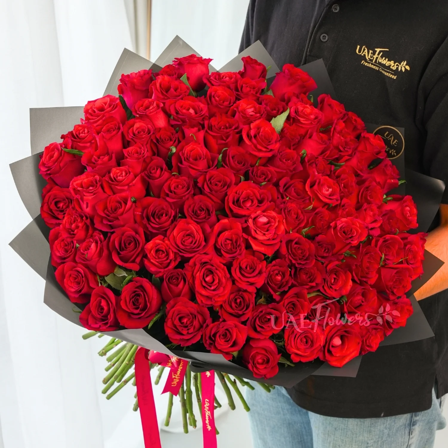 100 premium red roses hand-tied with green fillers and wrapped in black paper with satin ribbon
