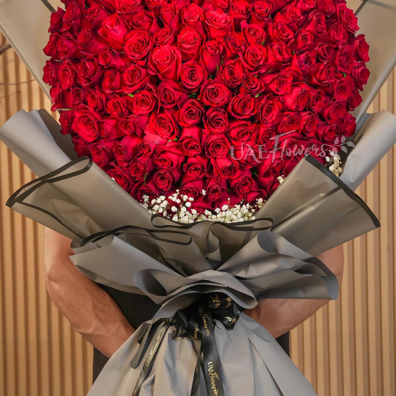Heart-shaped bouquet of 100 red roses with baby’s breath fillers wrapped in elegant black paper and ribbon