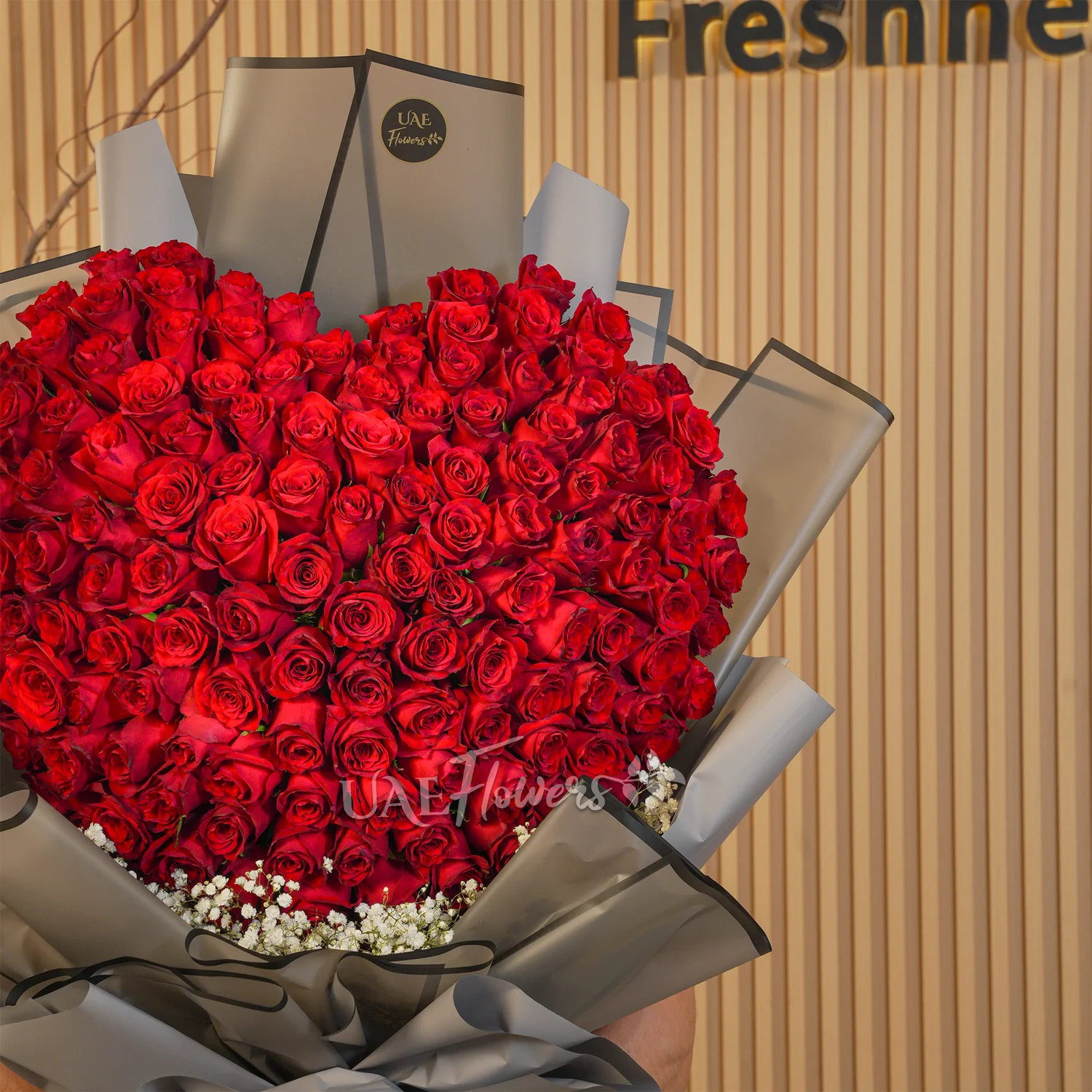 Heart-shaped bouquet of 100 red roses with baby’s breath fillers wrapped in elegant black paper and ribbon