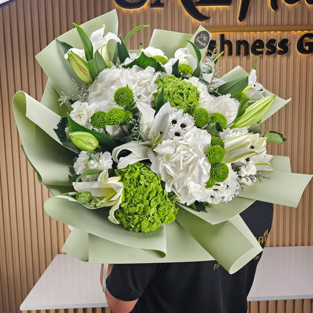 A bouquet of 2 white and 2 green hydrangeas, 5 white lilies and 2 green button chrysanthemums with green fillers and baby's breath in pastel green wrapping paper with white ribbon.