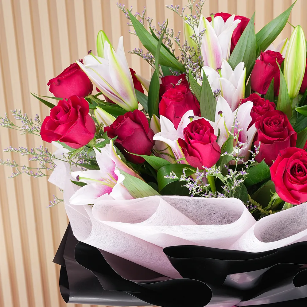 A bouquet of 4 pink lilies & 10 red roses in pink wrapping paper tied with a pink ribbon