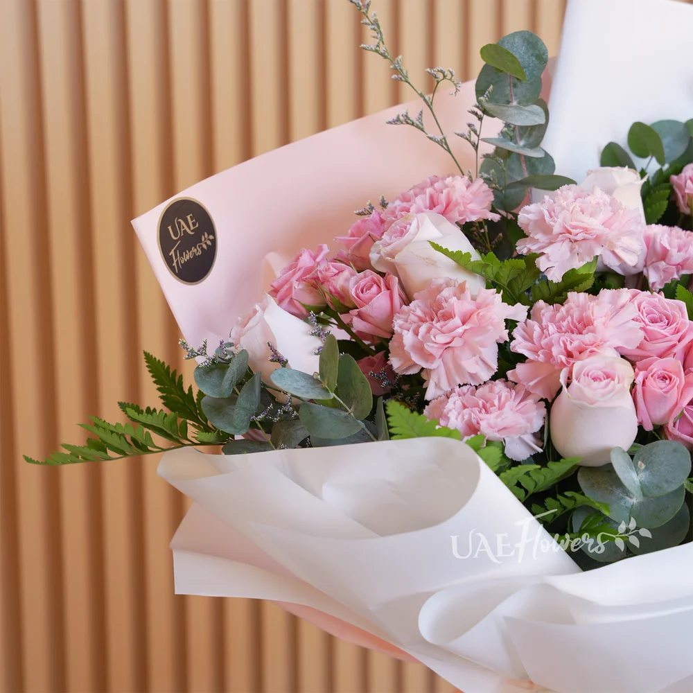 bouquet with 5 pink roses, 7 carnations, and 4 pink spray roses. Wrapped in paper with ribbons and green fillers.