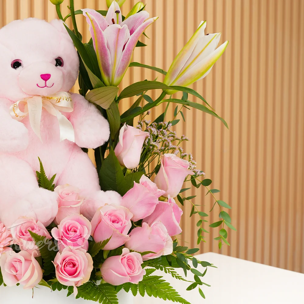 pink lily, pink gerberas, and pink roses in a round white box with a small pink teddy bear