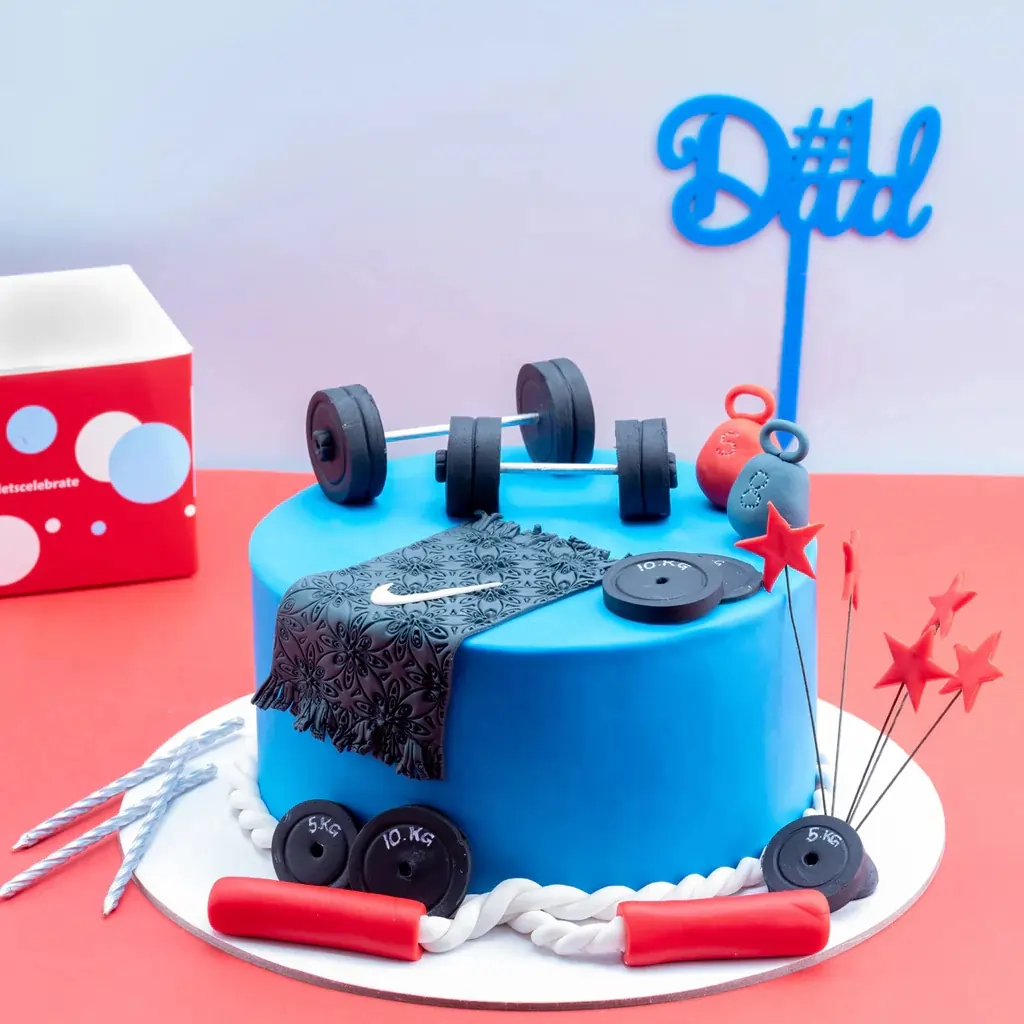 Blue fitness-themed cake decorated with fondant weights, a barbell, a Nike towel, kettlebells, and red stars, perfect for gym enthusiasts or fitness-inspired celebrations.