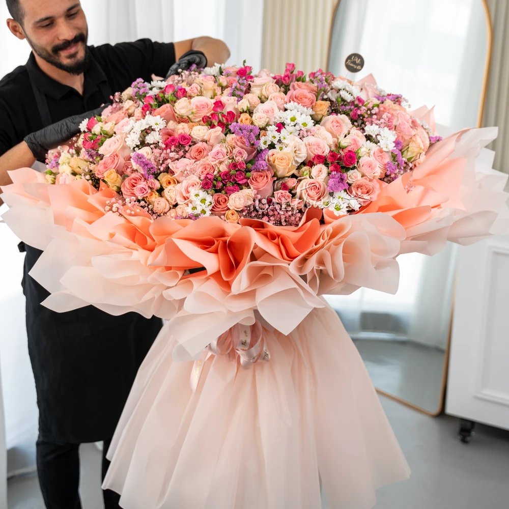 Grand bouquet of 70 mix color spray roses, 80 mix color roses and 10 white chrysanthemum with fillers in paper packing.