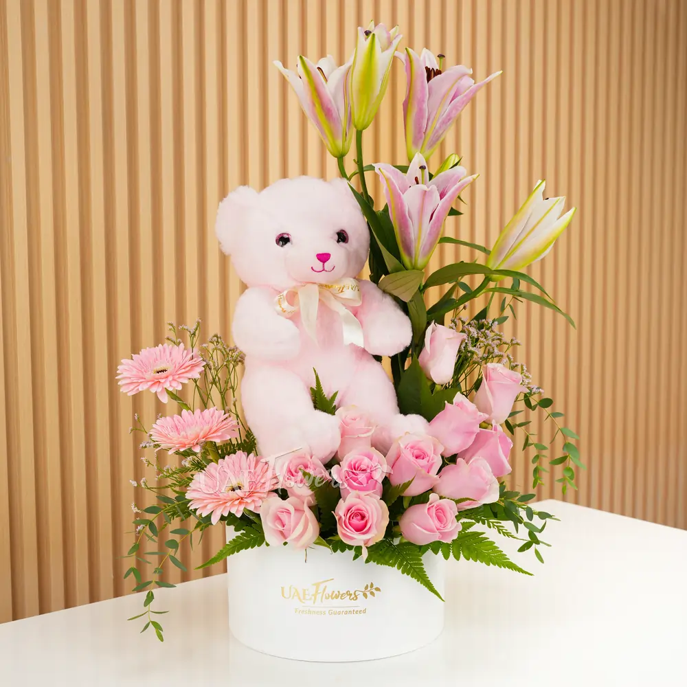 pink lily, pink gerberas, and pink roses in a round white box with a small pink teddy bear