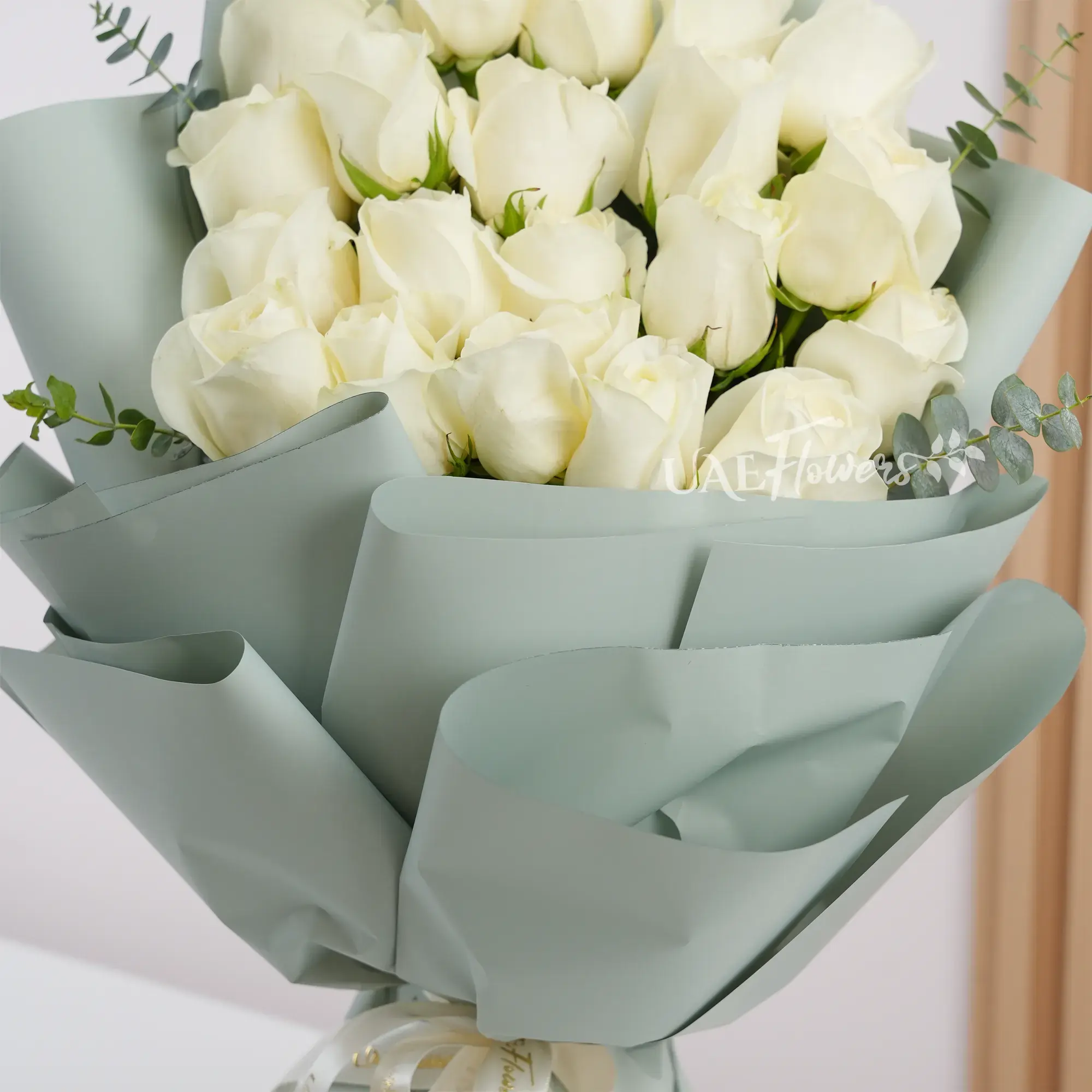 Bouquet of 20 white roses with green fillers wrapped in soft paper and tied with white ribbon, perfect for weddings, anniversaries, and special occasions.